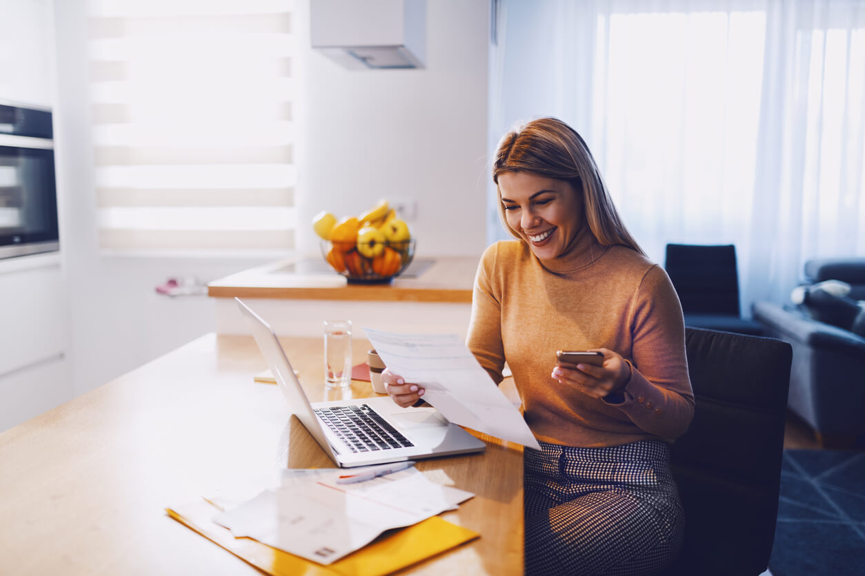 blonde woman looking at papers and laptop smiling