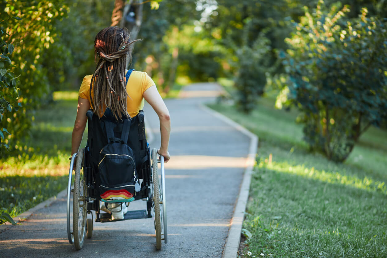 woman in a wheel chair rolling down a park path