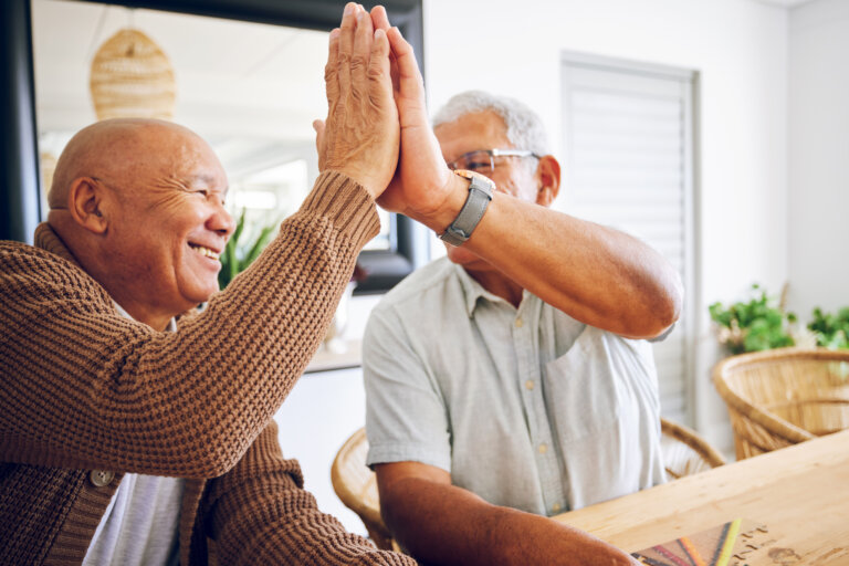 Two elderly men happily giving each other a high five indoors.
