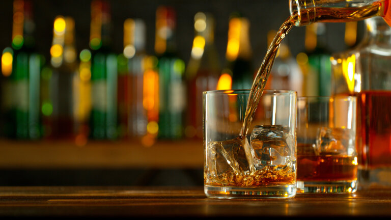 Close-up of pouring whiskey or rum on the bar, dark toned background