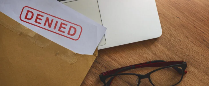 Document with denied stamp put on the laptop on wooden table,