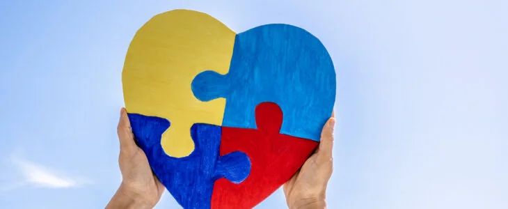 World autism awareness day, Autism spectrum disorder concept. Adult and child hands holding together colorful painted puzzle heart on blue sky background.